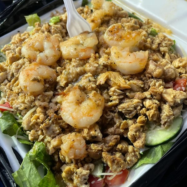 Shrimp and chicken salad with lettuce, tomatoes, and cucumbers in a white takeout container.