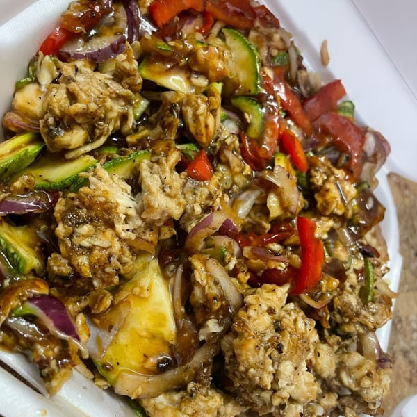 Close-up of a chicken salad with zucchini, red peppers, and red onions, drizzled with sauce.