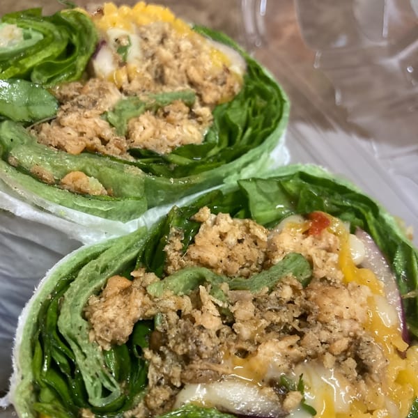 Two fresh WRAP-A-LOT wraps, filled with chicken, cheese, and vegetables, in a clear container.