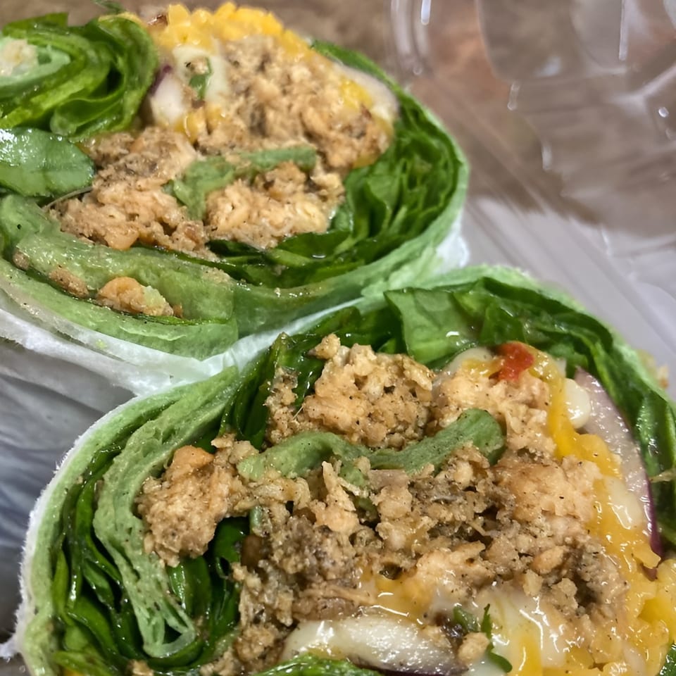 Two fresh WRAP-A-LOT wraps, filled with chicken, cheese, and vegetables, in a clear container.