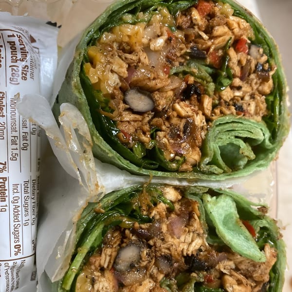 A close-up of a green spinach wrap, sliced in half, revealing chicken, black beans, and vegetables.