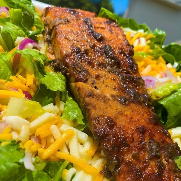 Grilled salmon fillet on a fresh salad with lettuce, shredded cheese, and red onions.