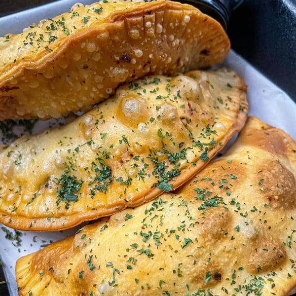 Three golden-brown, fried empanadas or calzones, sprinkled with green herbs, on a white paper-lined tray.