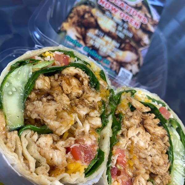 A chicken wrap from WRAP-A-LOT Fresh Express, cut in half, revealing chicken, lettuce, tomatoes, and cucumbers.